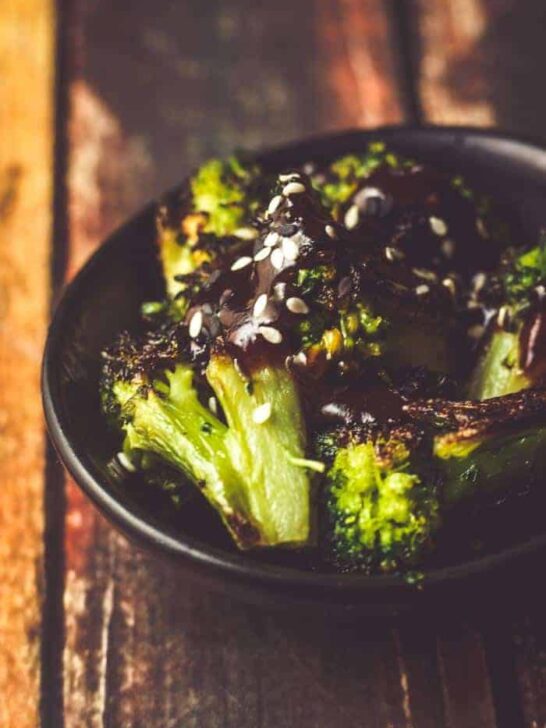 Roasted frozen broccoli with an easy asian sauce in a black bowl on a rustic wood table.