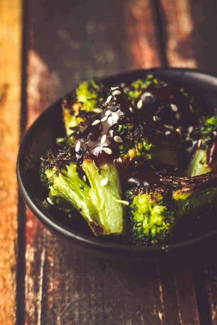Roasted frozen broccoli with an easy asian sauce in a black bowl on a rustic wood table.