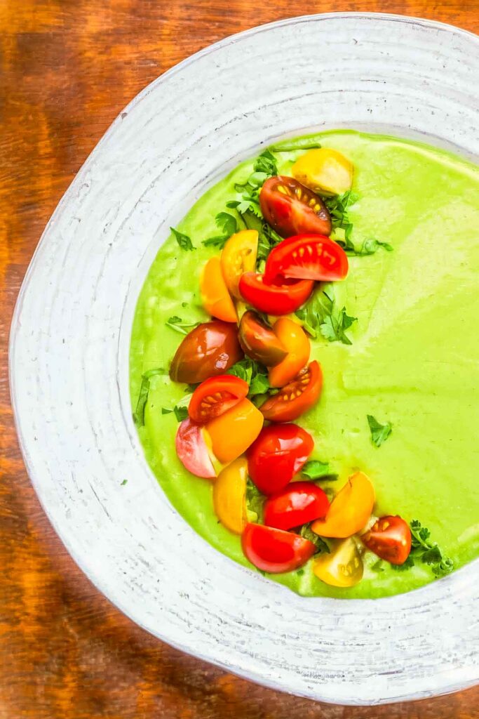 Avocado Soup (Cool, Creamy & Refreshing!) a closeup of a white bowl filled with avocado soup with quartered cherry tomatoes garnishing the left half of the soup