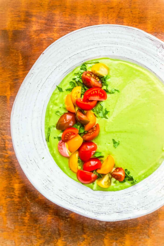 a white bowl filled with avocado soup with quartered cherry tomatoes garnishing the left half of the soup