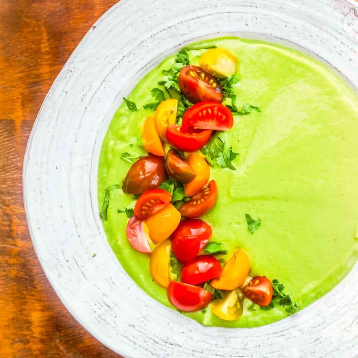 a white bowl filled with avocado soup with quartered cherry tomatoes garnishing the left half of the soup
