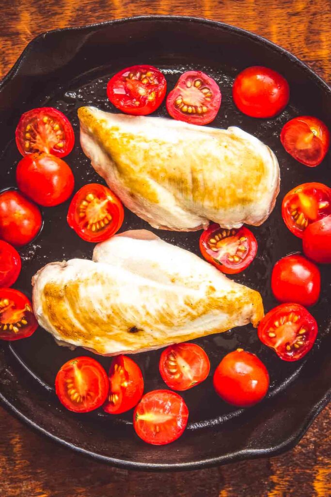 Air Chilled Chicken: Why It’s Better + A Recipe two air chilled chicken breasts being seared in a cast iron skillet with halved cherry tomatoes