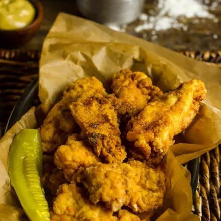 Pickle Brined Keto Fried Chicken in a basket with brown parchment paper and a pickle spear.