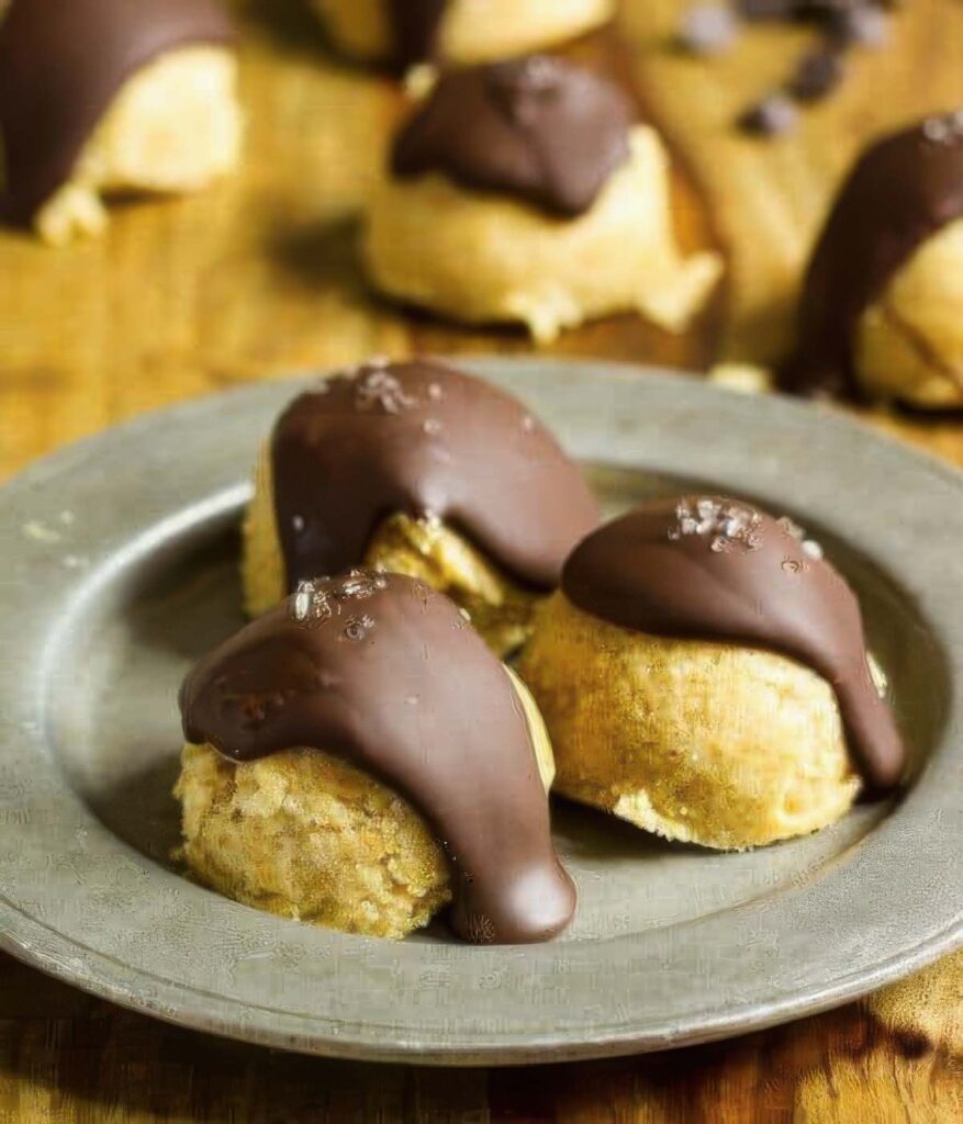 three keto cookie dough bites on a silver plate with a drizzle of chocolate with more bites in the background