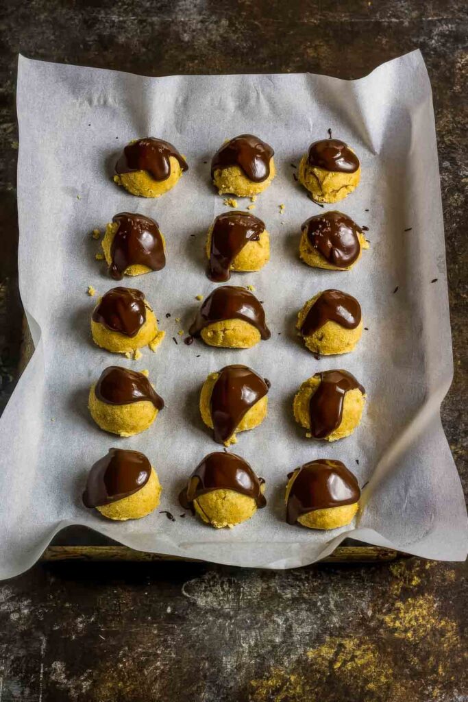 keto cookie dough bites on parchment paper on a sheet pan with a drizzle of chocolate