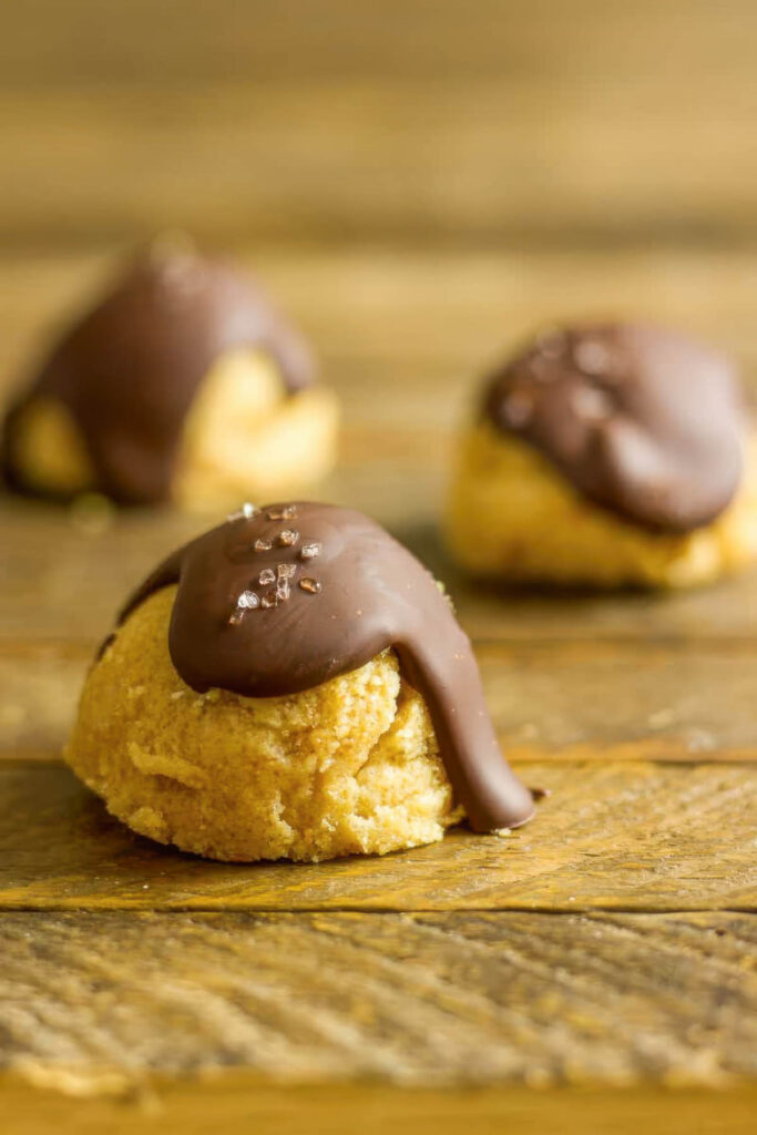 three keto cookie dough bites on a wooden table with a drizzle of chocolate