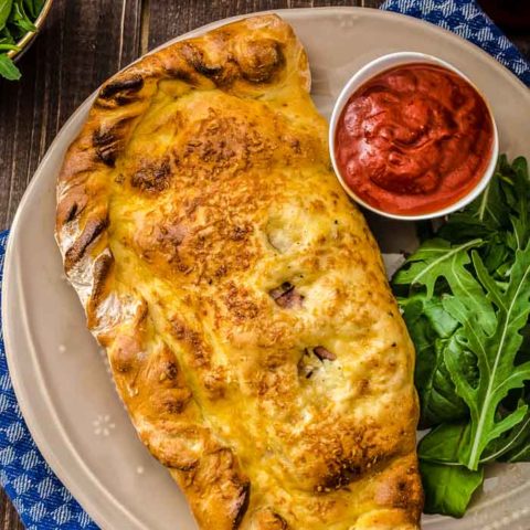 Pizza Dough Calzones on a table next to a cup of marinara sauce