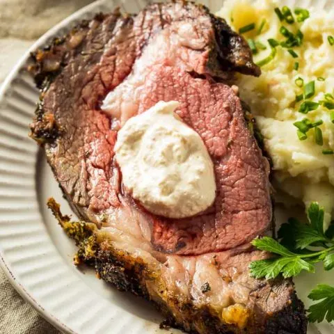 A slice of boneless prime rib on a white plate with mashed potatoes