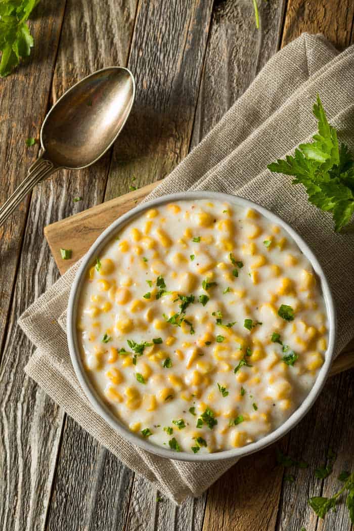 A bowl of creamed corn on a brown napkin and a wooden board