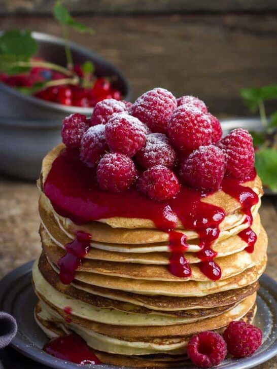 A stack of raspberry almond flour pancakes topped with fresh raspberries on a silver plate set on a wooden table