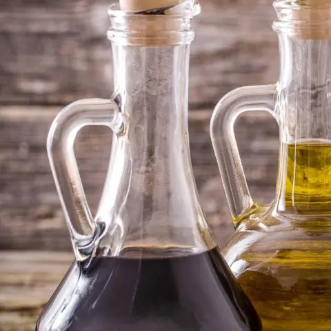 a bottle of balsamic glaze next to a bottle of olive oil on a brown table