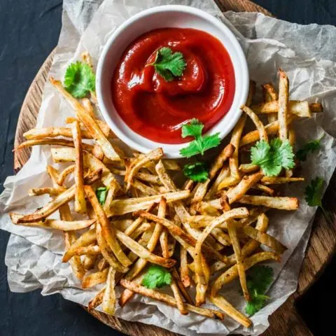 a plate of parsnip fries with a dish of ketchup on the side