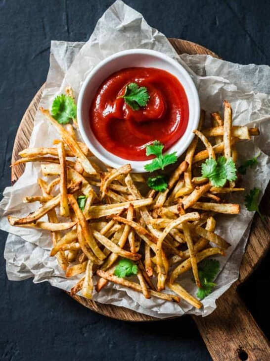 a plate of parsnip fries with a dish of ketchup on the side