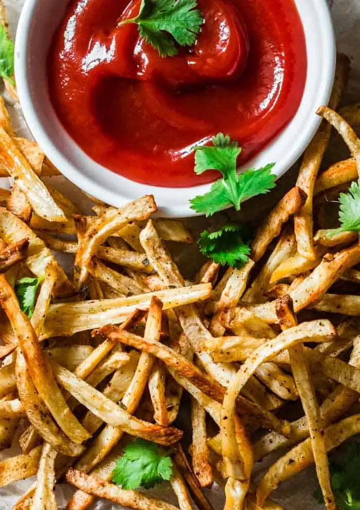 a plate of baked parsnip fries with a dish of ketchup on the side and sprinkled with chopped parsley