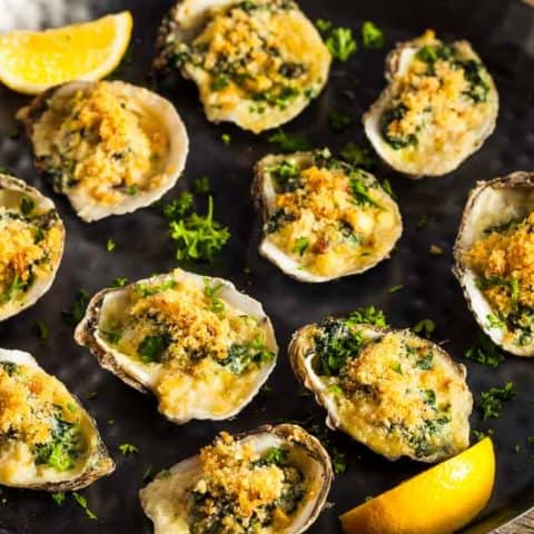 a platter of oysters rockefeller with lemon wedges as a garnish