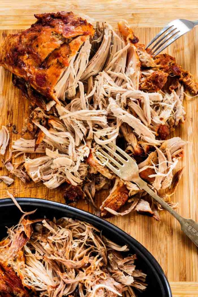 pulled pork on a cutting board with two forks and half of the roast ready to be pulled