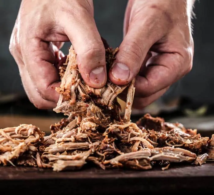 An example of pulling pork with your hands: pulled pork on a cutting board with a man's hands pulling apart a large piece of pork