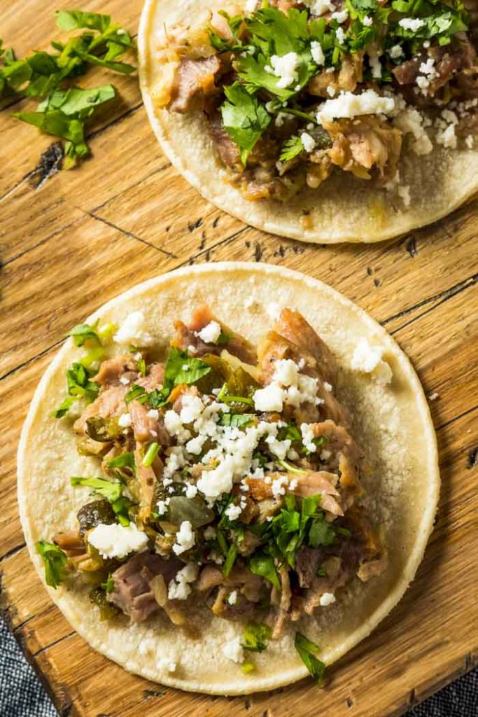 Pulled pork tacos on a cutting board with green salsa and queso fresco and Instant Pot Pulled Pork