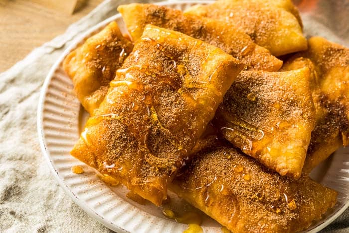 sopapillas on a white plate drizzled with cinnamon and honey