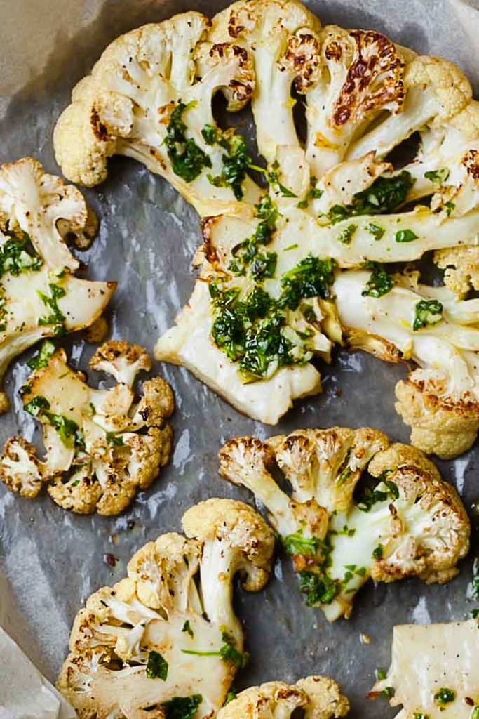 Roasted cauliflower steak with chimichurri sauce on parchment paper on a sheet pan