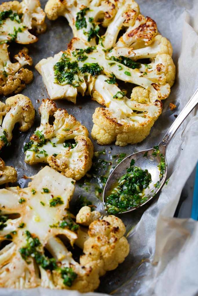 Roasted cauliflower steaks with chimichurri sauce on parchment paper on a sheet pan, just out of the oven