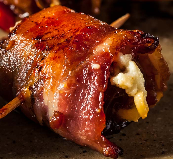 Closeup of a bacon-wrapped date with blue cheese on a brown plate
