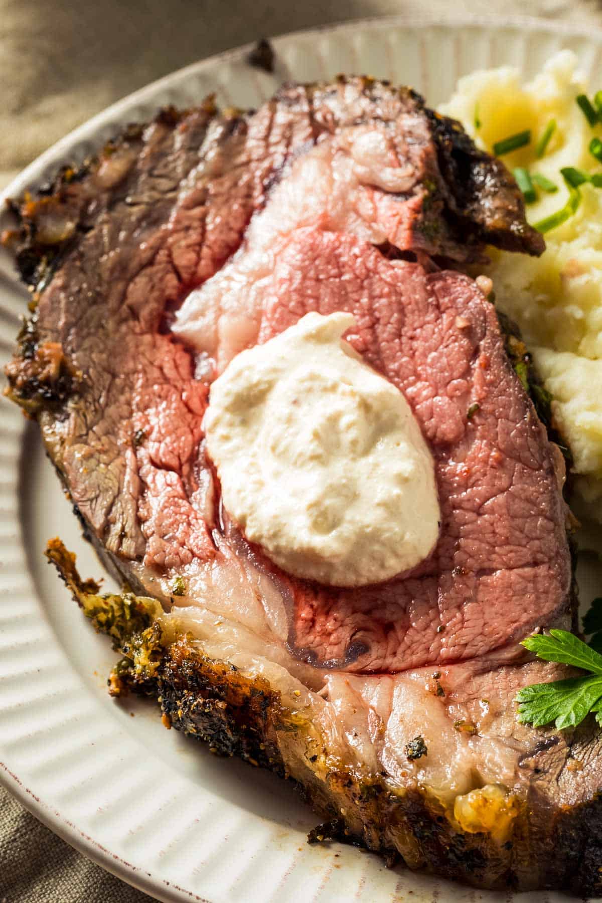 a closeup of a slice of boneless prime rib topped with creamy horseradish sauce, on a white plate