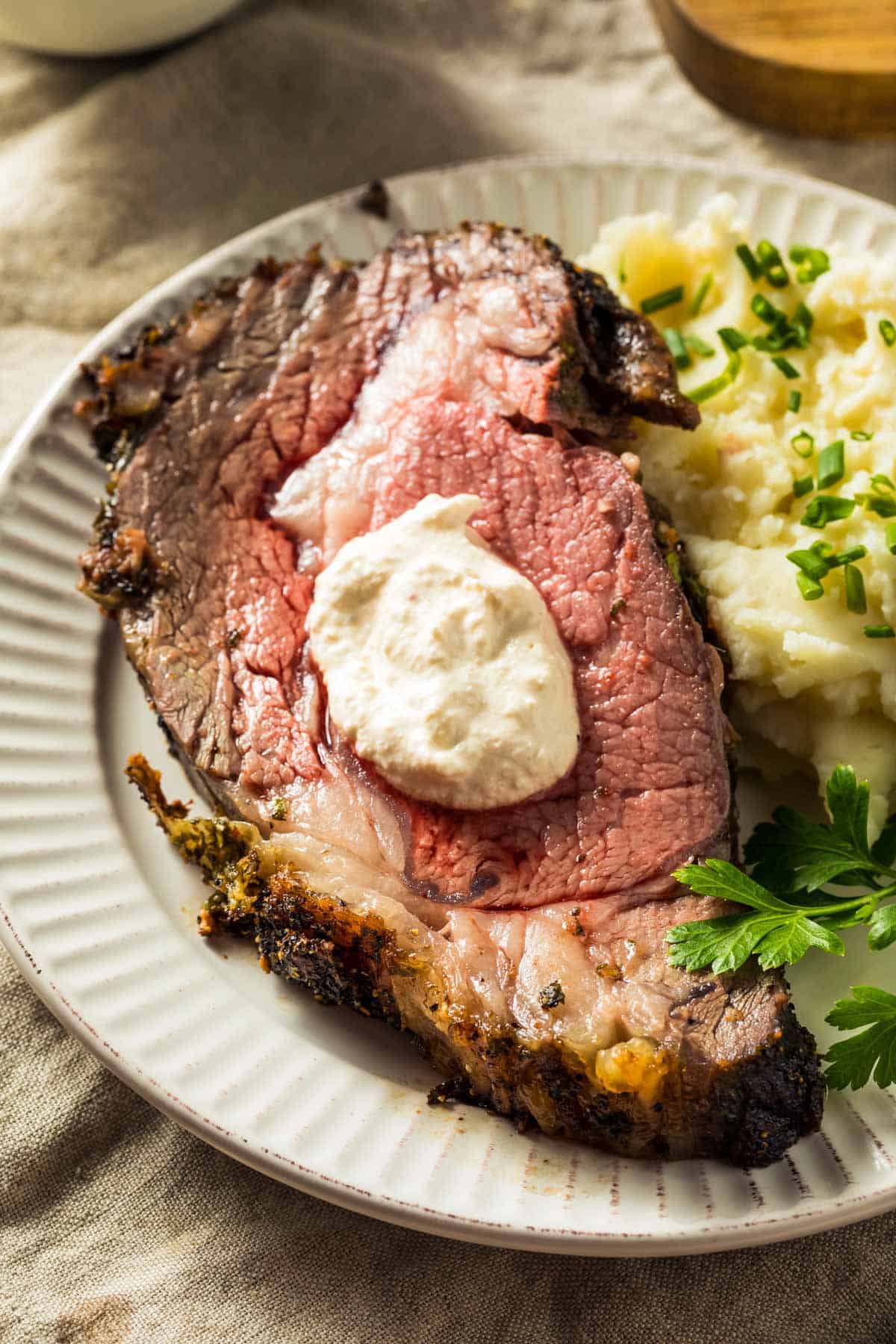 a slice of boneless prime rib topped with creamy horseradish sauce, on a white plate with mashed potatoes