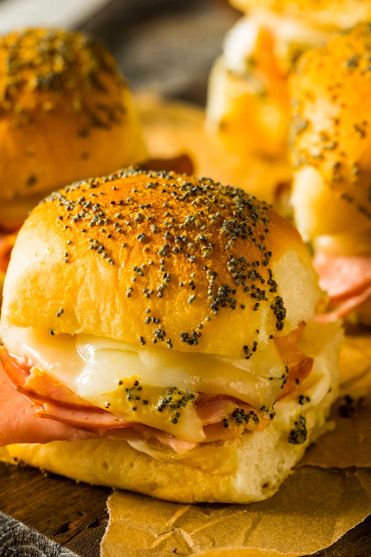 a closeup shot of ahawaiian rolls ham and cheese slider just out of the oven, placed on brown parchment paper