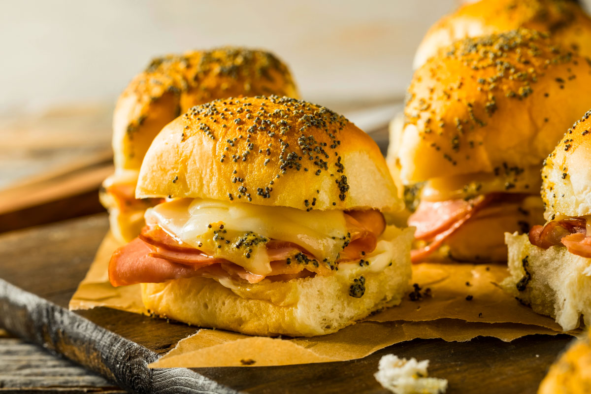 hawaiian rolls ham and cheese sliders just out of the oven, placed on brown parchment paper on a wood cutting board