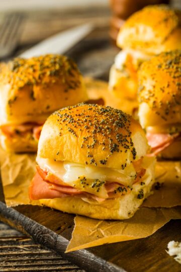 Hawaiian Roll Ham and Cheese Sliders a side view of hawaiian rolls ham and cheese sliders just out of the oven, placed on brown parchment paper on a wood cutting board