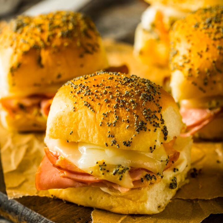 a side view of hawaiian rolls ham and cheese sliders just out of the oven, placed on brown parchment paper on a wood cutting board
