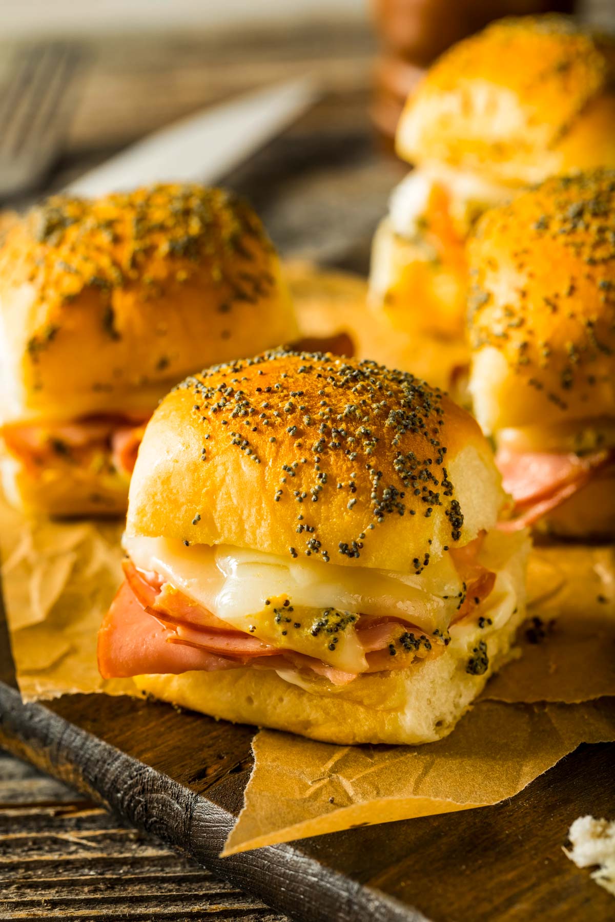 a side view of hawaiian rolls ham and cheese sliders just out of the oven, placed on brown parchment paper on a wood cutting board