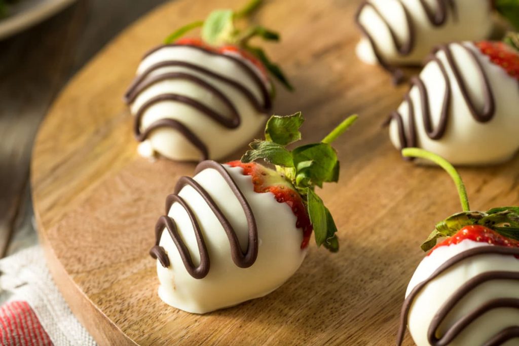 white chocolate covered strawberries drizzled with semi-sweet chocolate on a wooden board