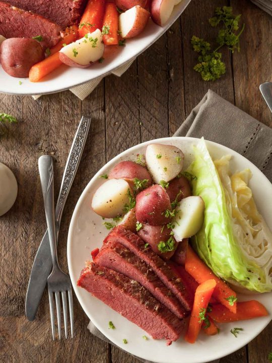 A plate of corned beef and cabbage with potatoes and carrots on a wooden table with a fork and knife