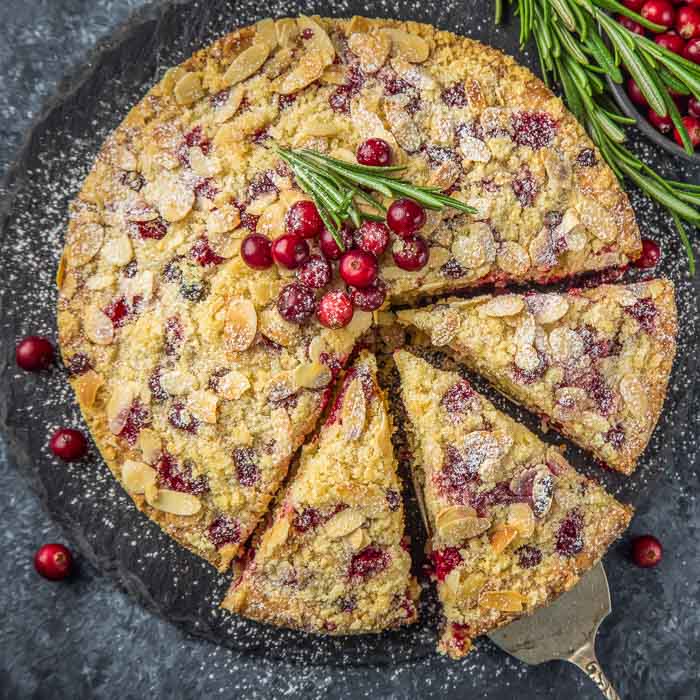 cranberry christmas cake topped with fresh cranberries and a sprig of fresh rosemary