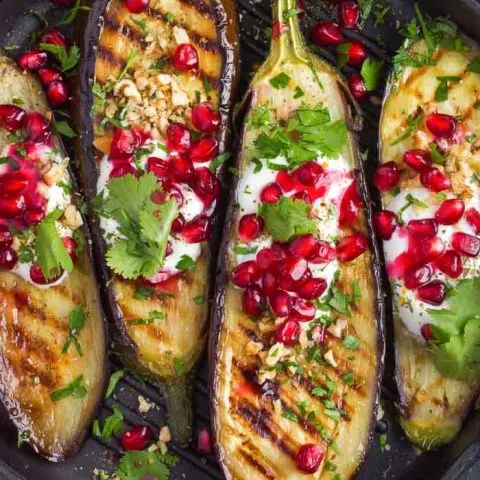 a closeup of grilled eggplant topped with garlic yogurt sauce, walnuts and pomegranate