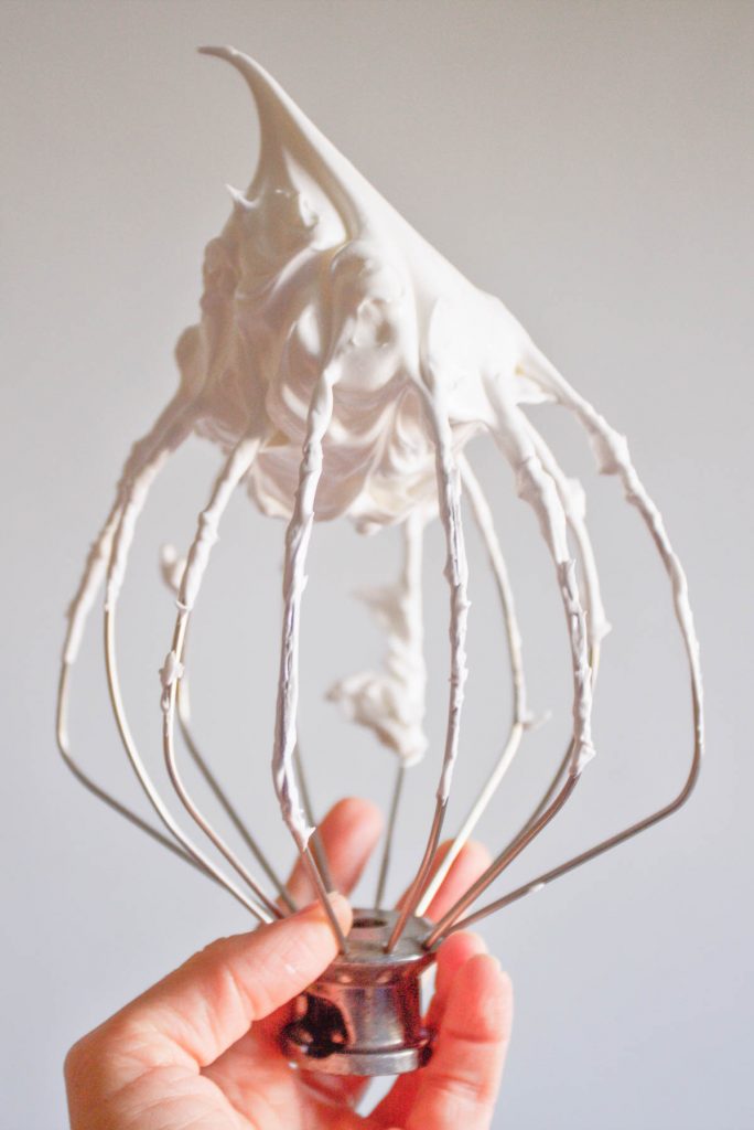 a hand with a beater with whipped meringue for christmas meringue cookies