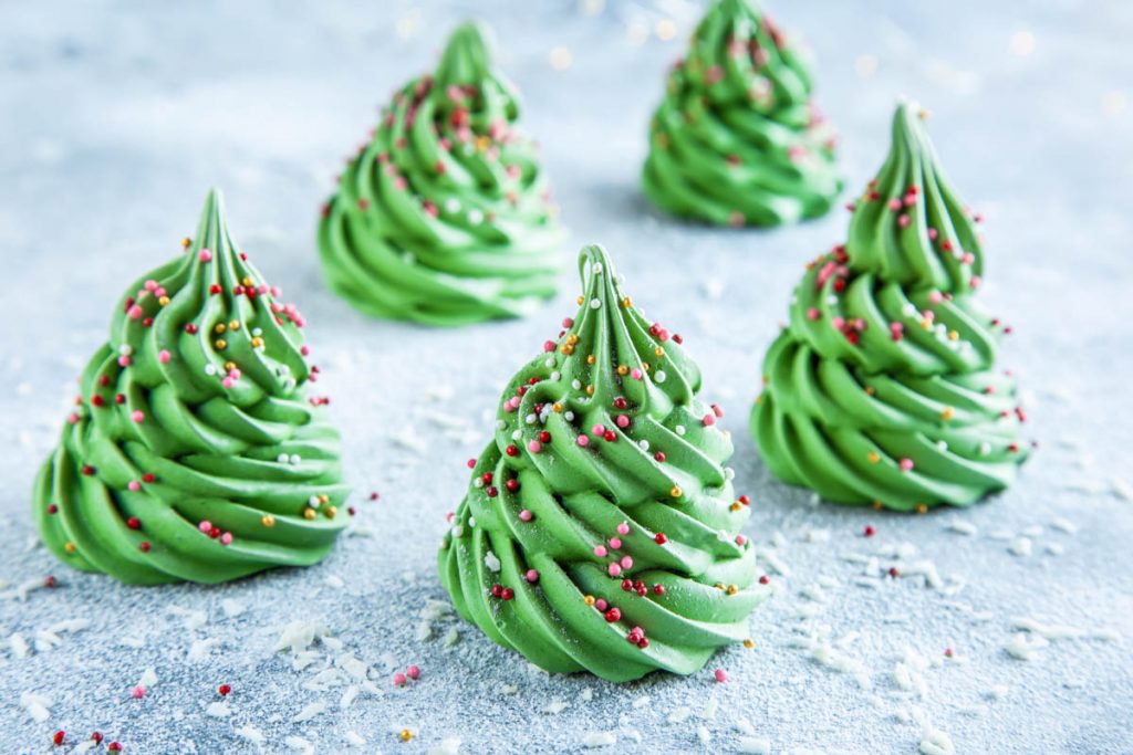 an assortment of meringue christmas trees with sprinkles on a light blue table with fake snow sprinkled on