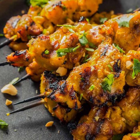 a closeup of a pile of thai chicken satay skewers on a round black plate