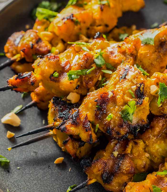 a closeup of a pile of thai chicken satay skewers on a round black plate