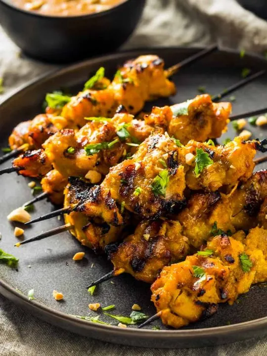 a pile of thai chicken satay skewers on a round black plate