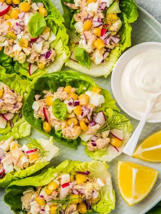 a closeup of tuna salad lettuce wraps with a small dish of mayo and lemon wedges