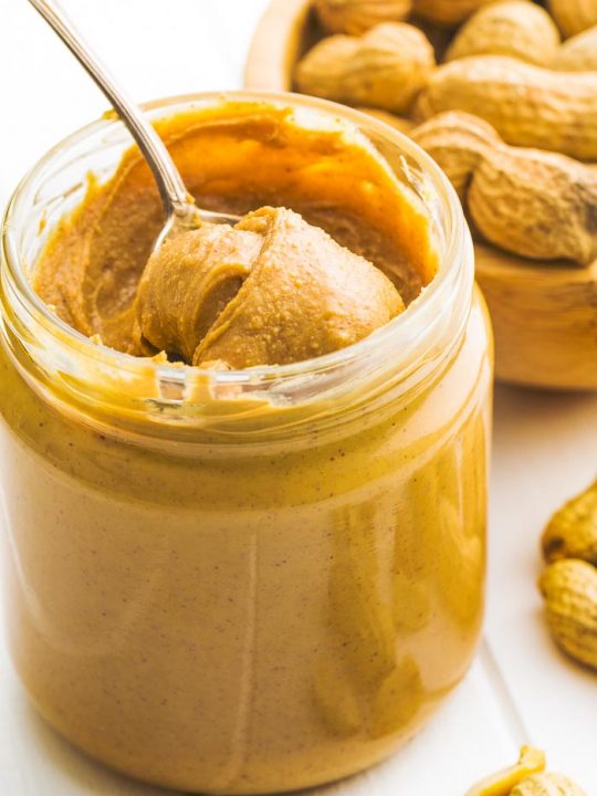 a jar of keto peanut butter on a white table with whole peanuts in the background
