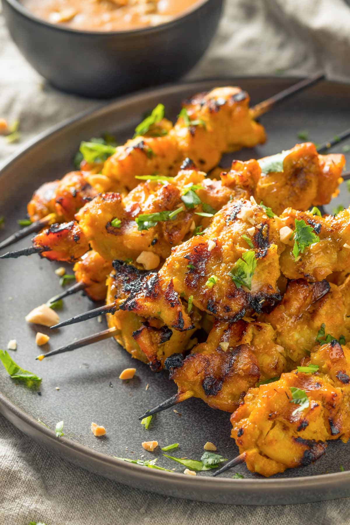 Chicken Satay Skewers + Peanut Sauce (Freezer-Friendly) a closeup of a black plate with a pile of chicken satay skewers on a tan linen napkin