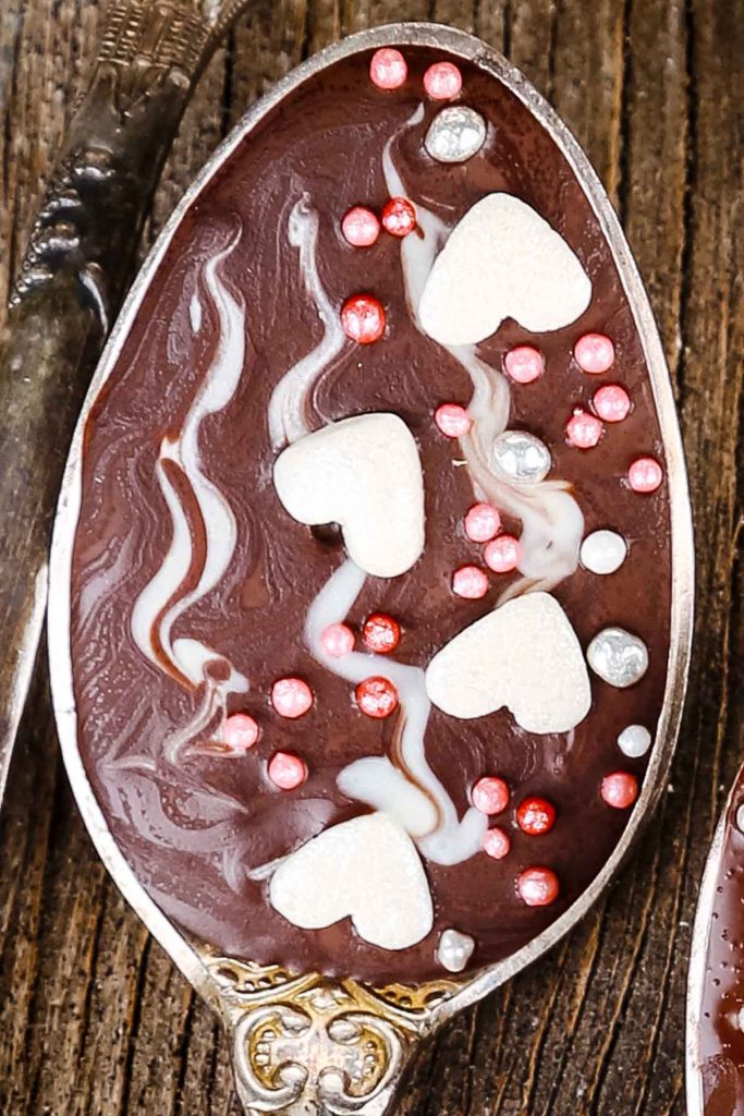 a closeup of a chocolate spoon with sprinkles, swirls, and four white hearts