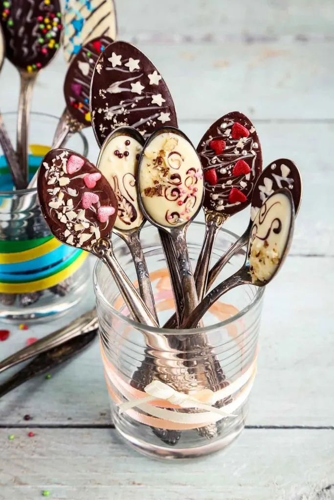 diy chocolate spoons with sprinkles, nuts, and hearts, set in a glass tied with ribbon