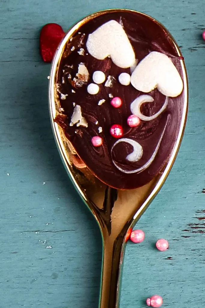 a closeup of a hot chocolate spoon with sprinkles and two white hearts