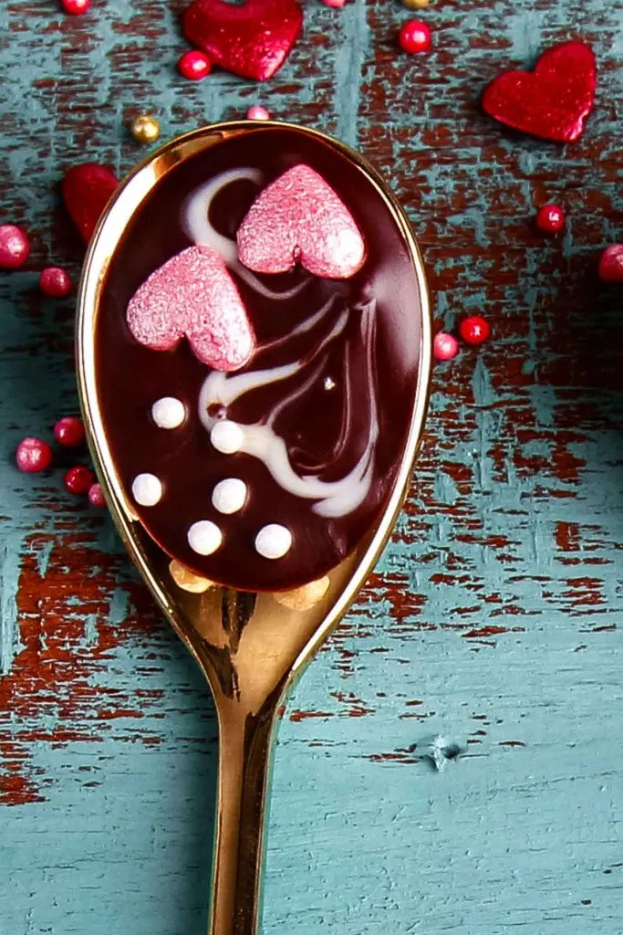 a closeup of edible chocolate dipped spoons with sprinkles and two pink hearts