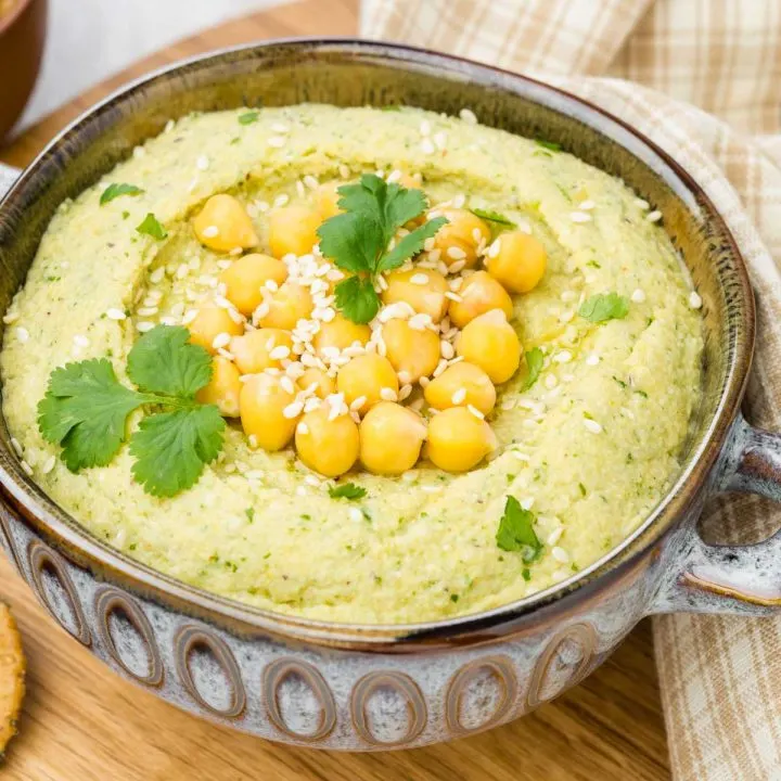 a bowl of cilantro jalapeño hummus on a wooden board with a small dish of garbanzo beans